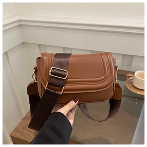 Detail of a brown faux leather saddle bag featuring a wide fabric strap and gold hardware
