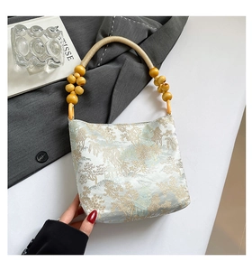 Detailaufnahme der blauen Brokatstickerei und des Holzperlengriffs an der Handtasche