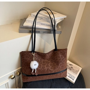 Detail of leopard print tote bag with plush charm and black leather handles in a cozy setting
