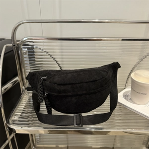 Minimalist black corduroy chest bag with adjustable strap on a modern display shelf