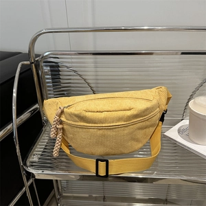 Minimalist yellow corduroy waist bag with rope zipper pull on transparent shelf