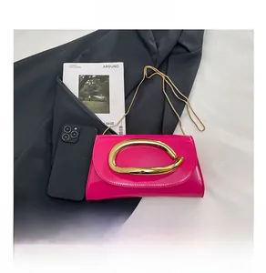 Detail of rose red patent leather shoulder bag with gold horseshoe buckle and chain strap