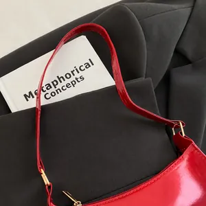 Close-up of red patent leather shoulder bag with gold buckle on a dark blazer