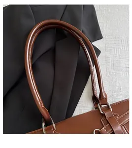 Detail of a brown leather shoulder bag featuring a reinforced handle and metallic ring hardware