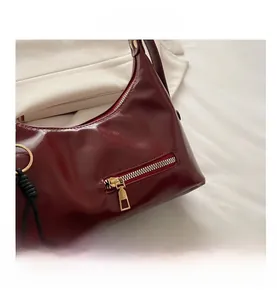 Detail shot of a dark red glossy leather tote with zipper pocket and beaded charm pendant