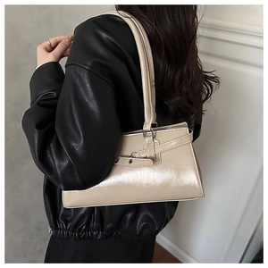 Close-up of beige glossy underarm bag with decorative buckle and strap detail