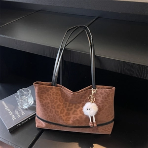 Chic leopard print tote bag with black handles and plush monster charm on a modern stand