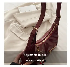 Detail view of adjustable gold buckle and glossy dark red leather strap on tote bag