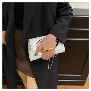 Close-up of white patent leather clutch bag with elegant gold arched handle and chain