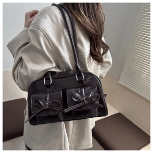 Detail of dark chocolate PU leather handbag with bows and shiny finish on the shoulder strap
