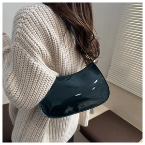 Detail of black patent leather hobo bag with glossy finish on a beige knit sweater