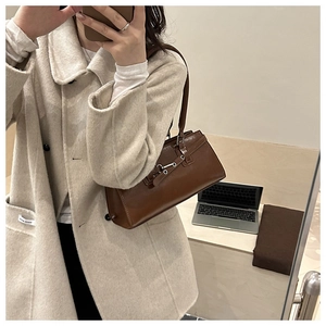 Close-up of brown vintage shoulder bag styled with a beige coat in an office setting