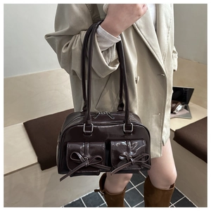 Detail of dark brown patent leather handbag with bow accents and twin front pockets