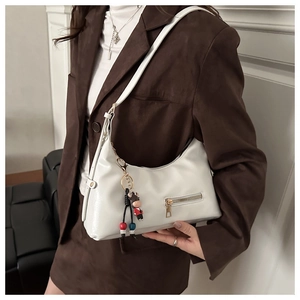 Close-up of a white faux leather hobo bag with zip pocket and cute doll charm on model