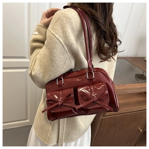 Detail of burgundy patent leather shoulder bag with decorative bows and front pockets