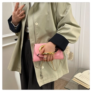 Detailed macro view of glossy pink clutch bag featuring a large gold metal ring handle