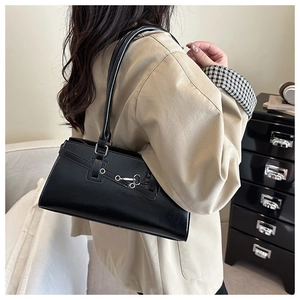Detail of black faux leather underarm bag with silver metal buckle on a beige trench coat