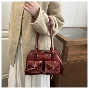 Detail of dark red patent leather shoulder bag with decorative bows and twin handles