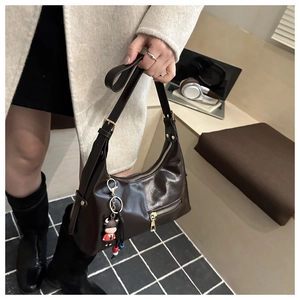 Detail of a dark brown crescent hobo bag with zip pocket and cute cow charm pendant