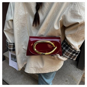 Detail of burgundy patent leather shoulder bag with gold oval buckle and chain strap