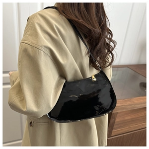 Detail of black patent leather underarm bag with gold zipper worn on beige blazer
