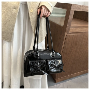 Detail of black faux leather ballet-style bag featuring bow pockets and glossy finish