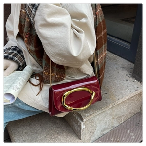 Deep red patent leather crossbody bag with a large gold metal buckle on a model