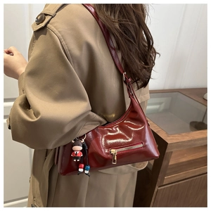 Detail of dark red glossy patent leather hobo bag with gold zipper and calf charm