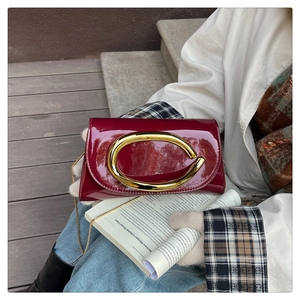 Detail of burgundy patent leather evening bag with oversized golden metal handle and chain