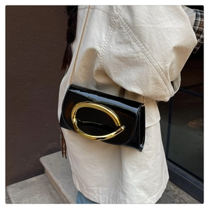 Close-up of black patent leather crossbody bag with oversized gold oval metal ring
