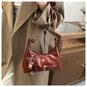 Close-up of deep red glossy tote bag with gold zipper detail and cartoon calf charm