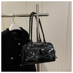 Close-up of black patent leather bag with bow knots and dual front pockets