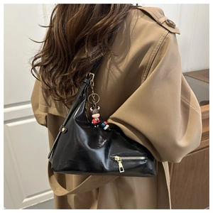 Close-up of black glossy tote bag with metal zipper and bull pendant worn by a model