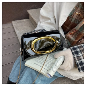 Detail of glossy black patent leather bag featuring a bold gold C-shaped metal buckle