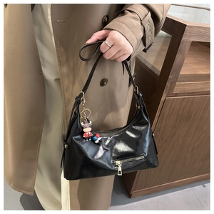 Detail of glossy black tote bag with mirror finish and cartoon cow charm keychain