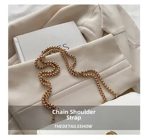 Detail of elegant gold box chain strap on a minimalist white handbag with metal finish