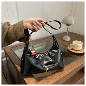 Detail of black glossy faux leather hobo tote bag featuring a cute red cow bag charm