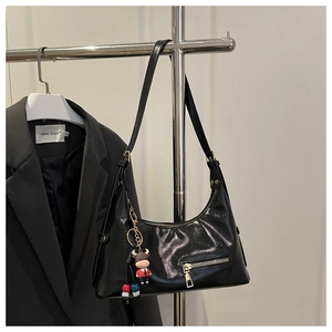 Close-up of a black glossy hobo bag with an adjustable strap and cartoon cow pendant