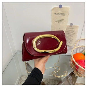 Detail of burgundy patent leather bag featuring a large gold C-shaped metal buckle
