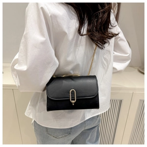Detail of minimalist black crossbody bag with gold oval clasp and chain strap on model