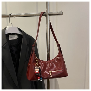 Deep red shiny leather shoulder bag with gold zipper detail and cartoon charm pendant