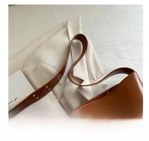 Dettaglio borsa a spalla in pelle lucida marrone con ampia tracolla con occhielli su blazer