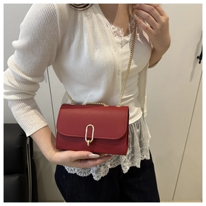 Red leather crossbody bag with gold oval lock and chain strap on a female model