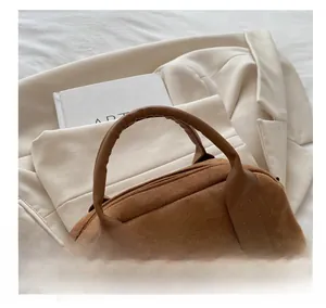 Detail einer braunen Wildleder-Boston-Tasche mit runden Griffen auf cremefarbenem Sakko