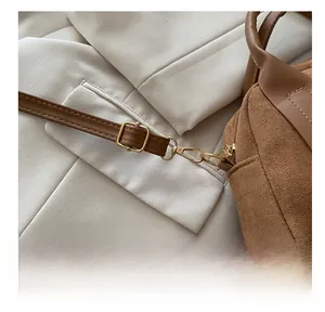 Detailaufnahme der goldenen Metallhaken und Schnallen an einer braunen Wildledertasche