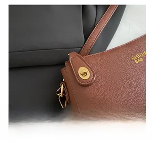 Close-up of brown litchi grain leather bag featuring a golden oval twist lock and metal hook