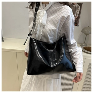 Dettaglio della borsa tote nera lucida con ampia tracolla decorata da occhielli in metallo