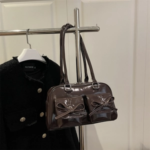 Dark brown patent leather shoulder bag with bow details and front pockets on a hanger