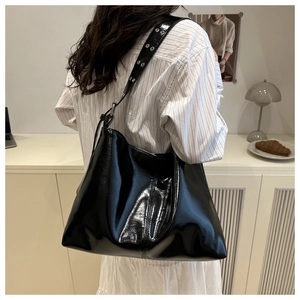 Dettaglio della borsa tote nera lucida con tracolla larga e occhielli in metallo argento