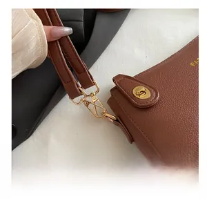 Close-up of golden hardware hook and litchi texture on brown leather crossbody bag